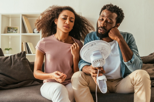 couple holding fan close to them & feeling warm due to poor air conditioner performance