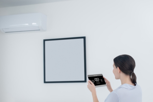 woman controlling ductless air conditioner using a tablet depicting ductless systems cost effectivity