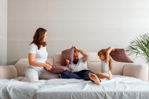 mom dad and young daughter pillow fighting in the living room depicting safe air conditioner