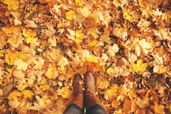 photo of woman's boots while standing in front of autumn leaves depicting end of summer