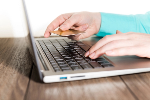 cropped view of a woman's hand while using a laptop and holding credit card depicting ordering oil